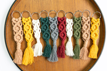 Hand made cotton macrame key chains of different colour on wooden dish , top view