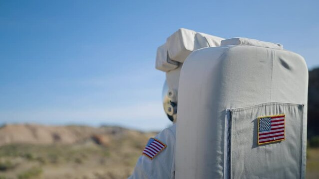 Astronaut looking around deserted terrain, equipped with a mirroring visor and space gear