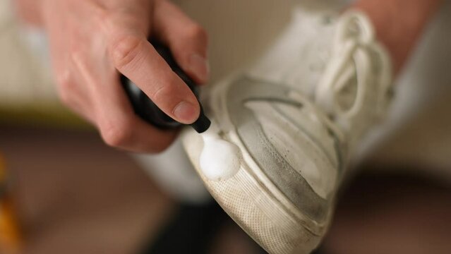 Male hands applying cleaning foam to dirty white shoes. Close-up of unrecognizable man wiping sole of sneakers from dirt and dust. Concept of caring for footwear. Shooting in slow motion.