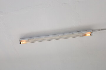 Old and damaged light bulbs. Dirty antique fluorescent light bulbs in a trough in a deteriorated concrete ceiling with light at the head and end of the bulb. Selective focus