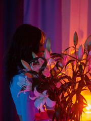 A beautiful young woman admires a bouquet of lilies. Portrait with a bouquet of flowers. Neon light