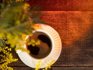 A cup of espresso coffee on a wooden table with a bouquet of yellow mimosas. Spring Postcard