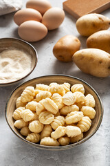 Front view of uncooked italian gnocchi. Behind view: potatoes, eggs, flour.