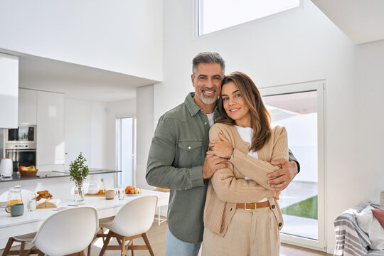 Happy smiling middle aged romantic affectionate couple mature older man and woman hugging standing at home together looking at camera enjoying bonding in modern house living room. Portrait. - Powered by Adobe