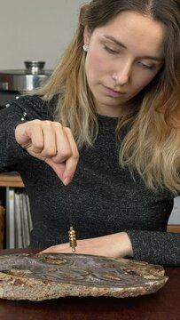 Woman using dowsing pendulum over big agate stone. Vertical video.
