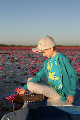Beautiful boy, fashion child, cute kid and lake with red lotuses in Udon Thani, Thailand. Nong Han Kumphawapi Lake or Red Lotus Lake (Talay Bua Daeng). Pink flowers, Thai nature, landmark. Scenery