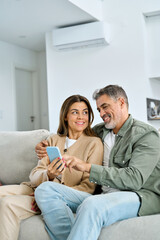 Happy older mature family couple, middle aged man and woman looking at cell phone using smartphone...