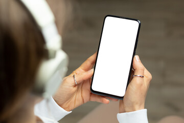 A woman in headphones holds a phone with a white screen listening to music. Smartphone mockup.