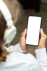 A woman in headphones holds a phone with a white screen listening to music. Smartphone mockup. - 728611173