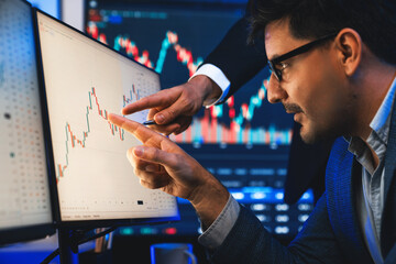 Stock trader pointing highest stock market on dynamic valued analysis with coworker on monitor real...