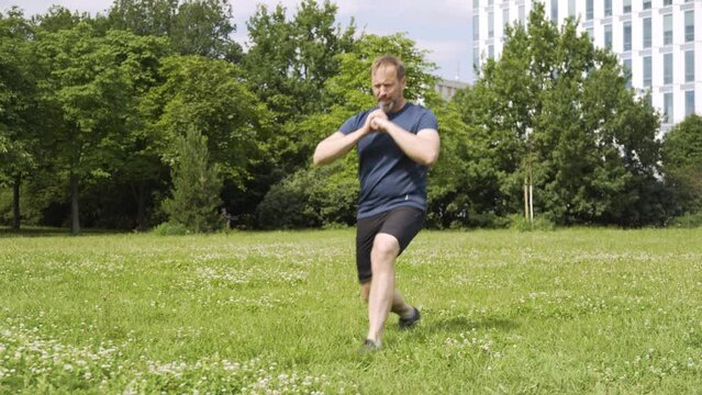 A handsome middle-aged Caucasian man does lunges in a park on a sunny day