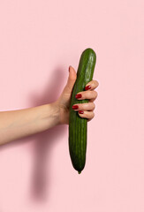 Woman's hand holds cucumber on pink background.