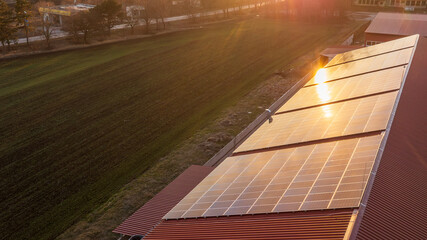 Aerial view of sunset light mirroring on solar panels on a building roof. Fotovoltaic panels...