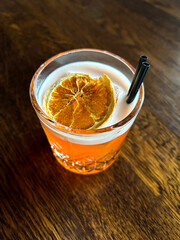 Alcoholic cocktail with orange in the drinking glass on the wooden background. Top view.