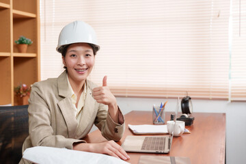 Confident Asian construction professional gives thumbs up, pleased with the progress on her laptop....