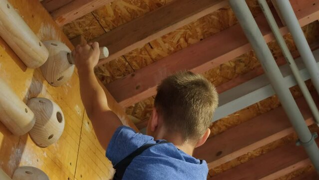 Strong boy reaches top of campus board using wooden grips at indoor climbing gym. Boy climber trains basic patterns of movement