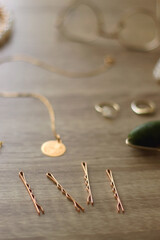 Pearl headband and barrette, golden eyeglasses, gold necklace, earrings and rings, jade face roller and hair pins on wooden background. Various elegant gold accessories. Selective focus.