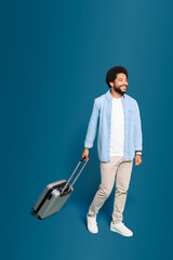 A dynamic scene as Brazilian young man in casual outfit walks with his suitcase isolated on blue, active lifestyle of a young traveler in motion, ready for new experiences