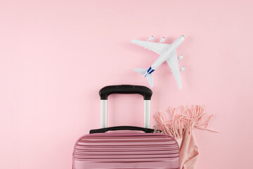 Awakening adventures: roaming in the season of renewal. Top view photo of suitcase, cozy scarf, model of plane on pastel pink background