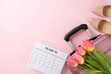 In full bloom: a traveler's spring odyssey. Top view photo of suitcase, calendar, heels, fresh tulips on pastel pink background with marketing zone