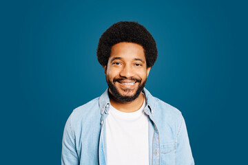 Cheerful Brazil man stands with a confident smile against blue backdrop, exuding warmth and a down-to-earth personality. This shoot emphasizes friendly confidence and the simplicity of modern attire