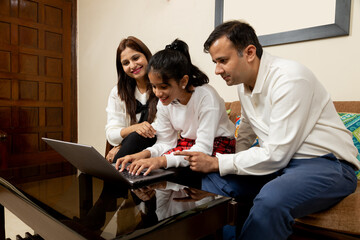 Indian Girl with mother and father using laptop while sitting on Sofa in Living room at home