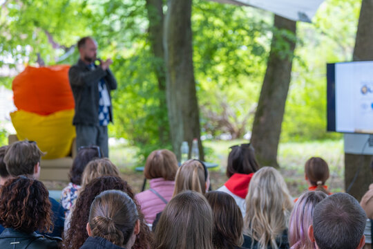 Focused audience listening to a speaker at an outdoor educational workshop surrounded by trees.