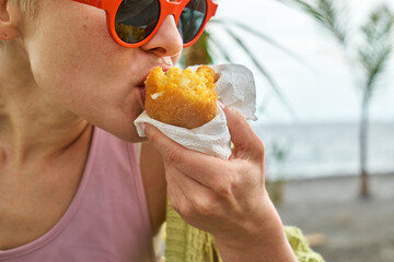 Young blond woman at seaside eating hot palatable arancini (deep fried rice balls with meat)....