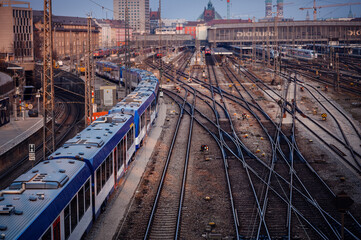A commuter train moves along the complex railway tracks in an urban setting at dusk