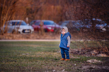 A curious toddler in a hooded jacket stands alone in a park during the early winter