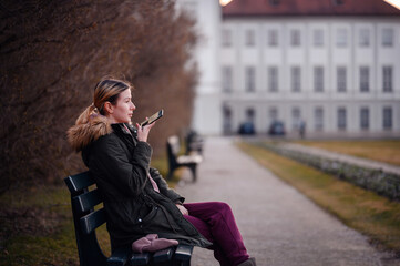 Woman converses on a smartphone while seated on a park bench, a wisp of breath visible in the cool air