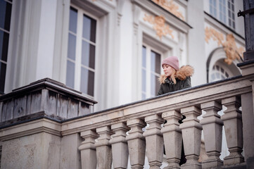 A pensive woman leans on a classic stone balcony, gazing out over the historic cityscape