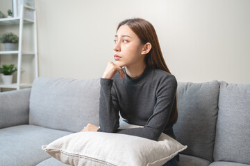 Unhappy anxiety young Asian woman covering her face with knee on the sofa in the living room at...