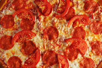 Baked pepperoni and tomato pizza sits invitingly on a wooden serving board. Texture