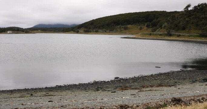 Pan of Estancia Harberton and the Beagle Channel ocean in Tierra del Fuego, Patagonia Argentina. View of the rocky shore, houses and hills in a cloudy day. 