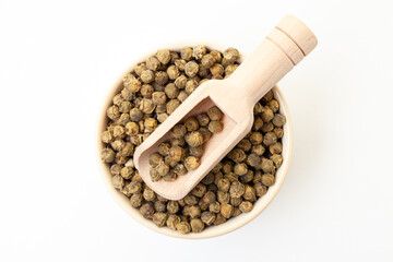 Green peppercorns in bowl with wooden scoop on white background. Dry white pepper grain