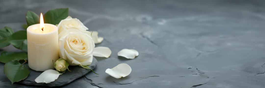 White candle with a rose and flowers petals on grey stone panoramic background with copy space, funeral web banner