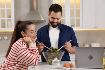 Happy lovely couple cooking together near laptop in kitchen