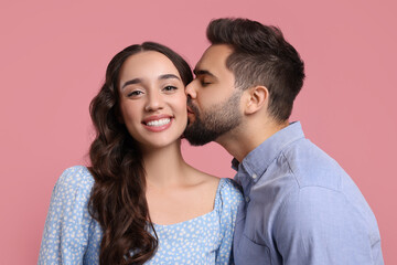 Man kissing his smiling girlfriend on pink background