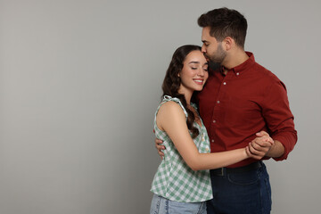 Man kissing his smiling girlfriend on grey background. Space for text