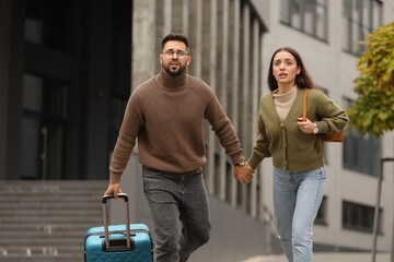 Being late. Worried couple running near building outdoors - obrazy, fototapety, plakaty