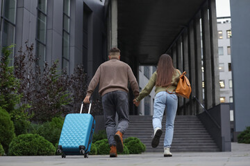 Fototapeta premium Being late. Couple with suitcase running towards building outdoors, back view
