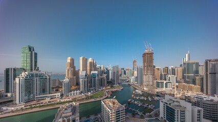 Dubai Marina with several boats and yachts parked in harbor and skyscrapers around canal aerial all day timelapse.