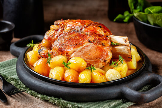 Black board with served pork shank or knuckle with baked baby potato. German, austrian, italian food.