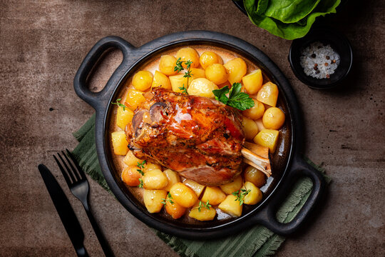 Top view of pork knuckle or shank with potato. Baked pork leg, German food on a brown table.