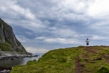 Fototapeta na wymiar A path leads to the Borhella lighthouse, a solitary figure against a dramatic sky, on Norway's rugged coastal landscape