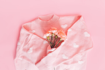 Pink jacket with white hearts hugs a bouquet of flowers on a pink background.