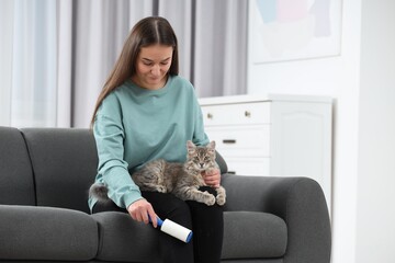 Pet shedding. Woman with lint roller removing cat`s hair from trousers on sofa at home, space for text