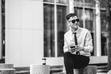 Urban business lifestyle: modern and young professional with white shirt and black tie using a phone in business district (in black and white)