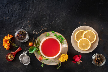 Tea with different ingredients and copy space. Herbs, fruits, and flowers, overhead flat lay shot on a black slate background